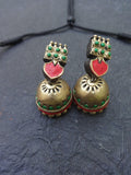 Pair of traditional Terracotta earrings with red and green accents on a dark textured surface