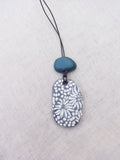 Necklace with a blue Terracotta pendant and white floral pattern on a light gray background