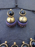 Pair of gold and purple terracotta  terracotta earrings on a textured dark blue surface