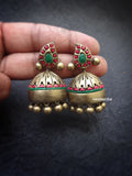 Ornate gold terracotta earrings with red and green accents held by a hand on a dark background.