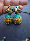 Gold and turquoise terracotta earrings held between fingers on a dark surface