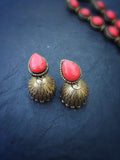 Pair of terracotta earrings with red coral stones and gold-colored bases on a dark blue background