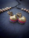 Pair of gold jhumka terracotta  earrings with red and blue accents on a dark surface