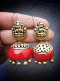 Gold and red terracotta earrings held between fingers against a dark background