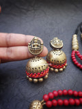 Brass jhumka  terracotta earrings with red stones held by a hand on a dark background