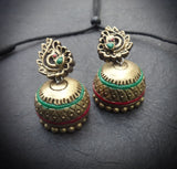Pair of ornate brass terracotta  earrings with green and red accents on a dark surface
