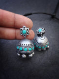 Silver and turquoise terracotta earrings held between fingers on a dark background