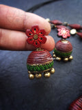 Red and green terracotta earrings with floral design held by a hand on a dark background