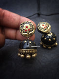 terracotta black and gold earrings with red stones held by a hand on a dark background.