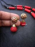 Red and gold terracotta  earrings held by a hand on a dark background with 'Nakshatra' branding.