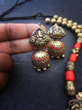 terracotta  gold and red earrings held by a hand on a dark surface