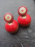 Red terracotta earrings with gold accents on a textured gray surface