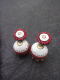 Pair of terracotta  earrings with red and white design on a dark textured background