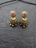Pair of gold terracotta earrings with green and red stones on a dark textured surface