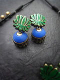 Pair of terracotta earrings with green leaf-like tops and blue round bases on a dark textured surface.