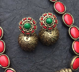 Pair of gold terracotta earrings with green and red stones on a dark textured surface