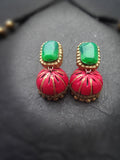 Pair of terracotta earrings with green gemstones and pink and gold designs on a dark background