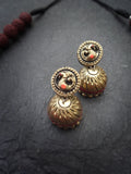 Gold terracotta earrings with intricate designs on a dark textured surface