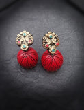 Red terracotta earrings with gold and gemstone details on a dark fabric background