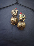 Pair of ornate gold terracotta earrings with peacock design on a dark background